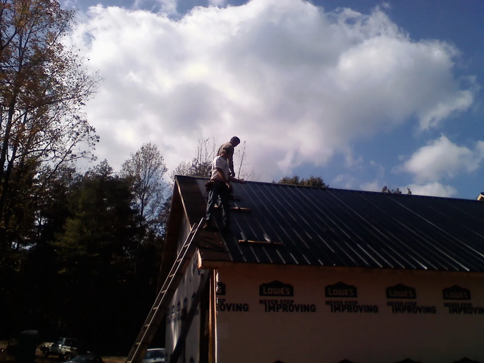 Roofer fastening dark metal panels high against a cloudy sky, from a Roof Inspection job in Woodbury