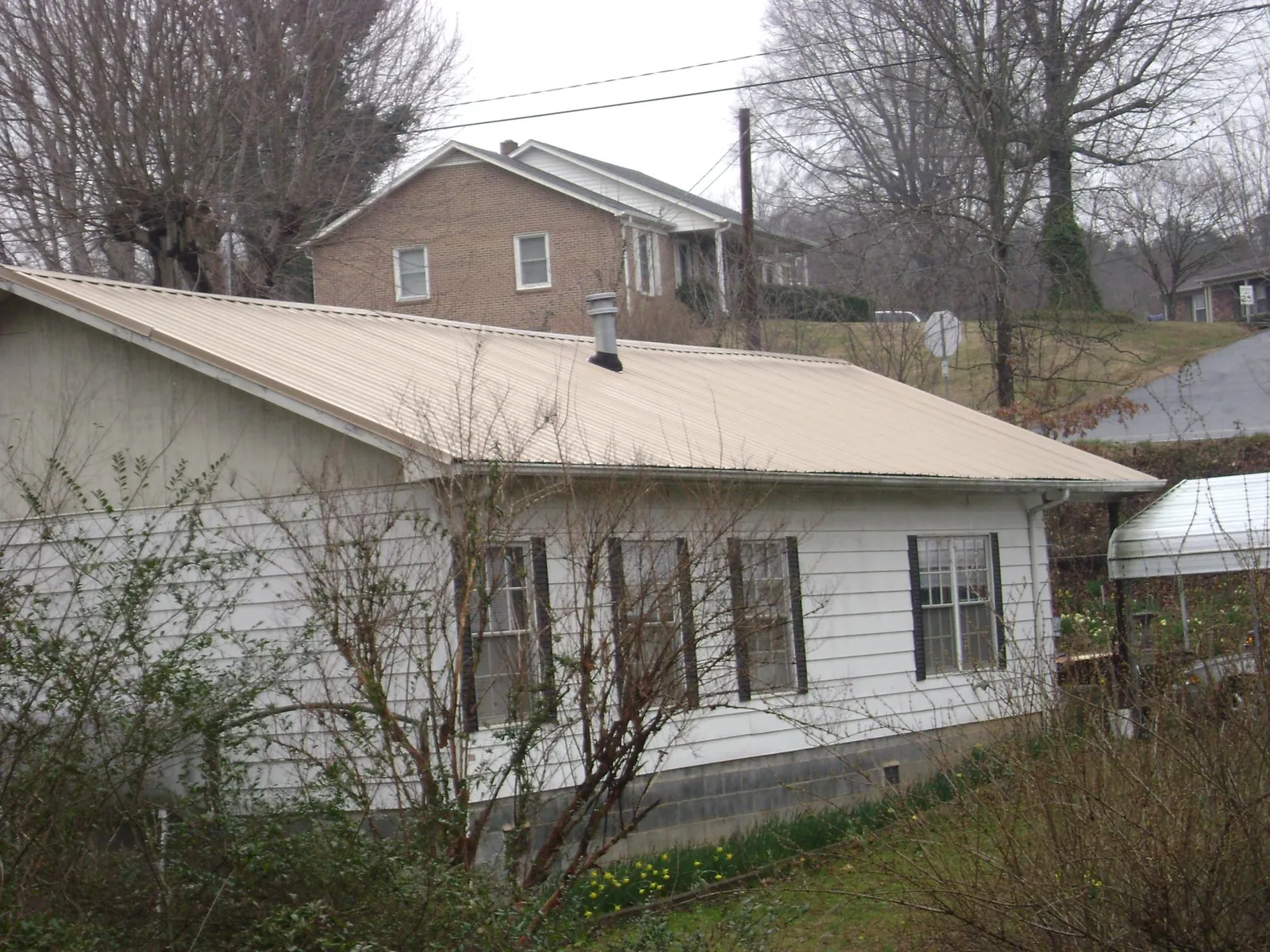 Tan metal roof on a white sided house set into a hillside — Commercial Roofing by Roofing Brothers in Woodbury
